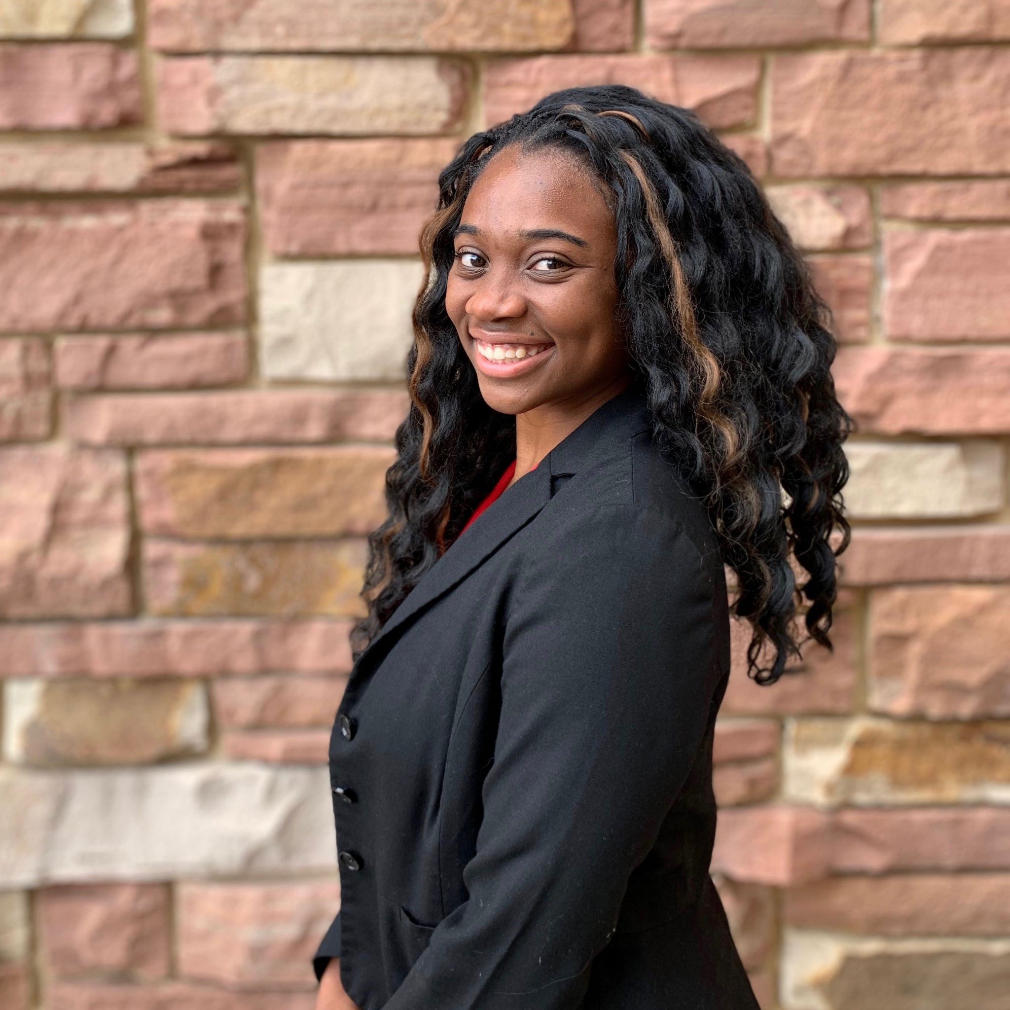 Photo of a female in business suit posing in front of a brick wall